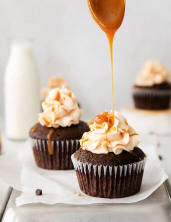 Caramel being drizzled on top of frosted chocolate cupcakes