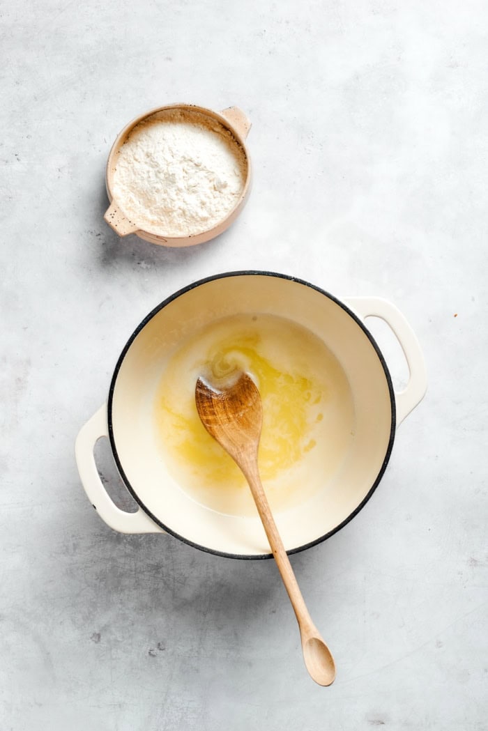 Overhead view of liquid mixture in pot with wooden spoon and flour in bowl