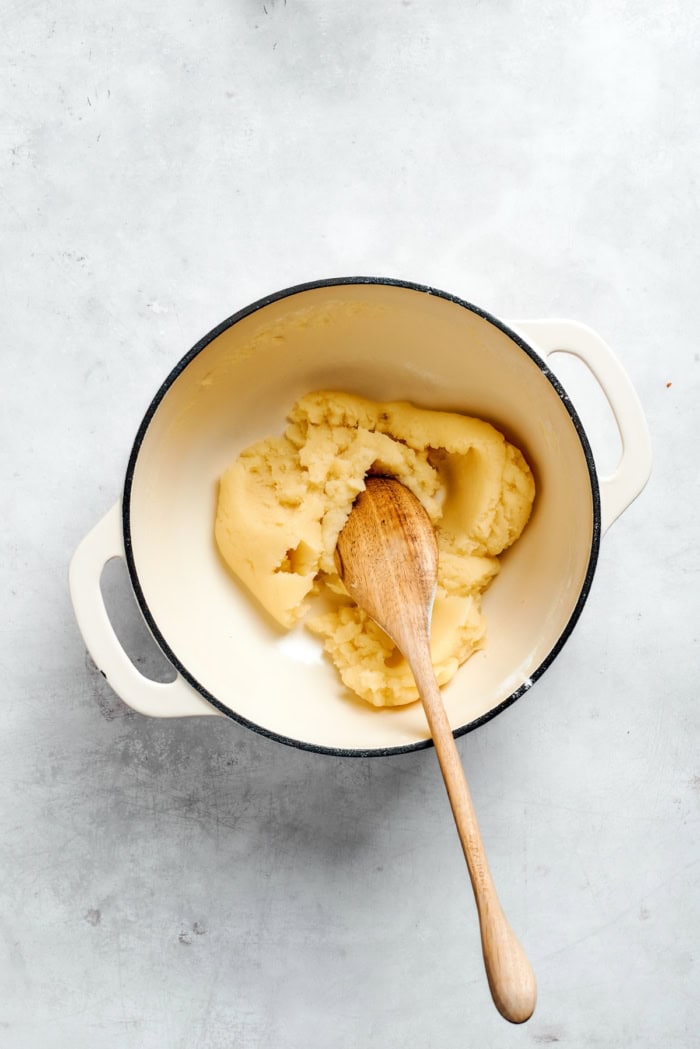 Overhead view of choux dough mixture in pan with wooden spoon