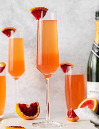 Blood orange mimosas next to a bottle of champagne