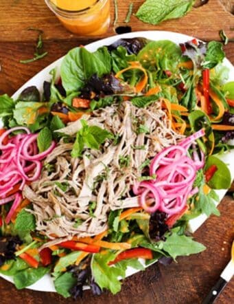 A platter of Banh Mi Salad with greens, sliced vegetables, pickled red onions, shredded meat and Sriracha vinaigrette dressing