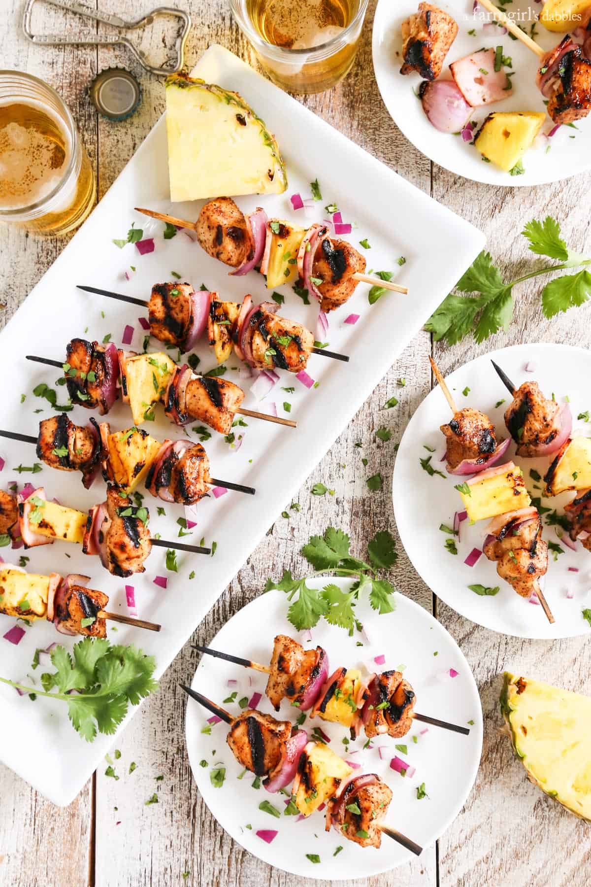 Grilled Hawaiian Chicken Chili Kebabs on a white platter and plates with glasses of beer