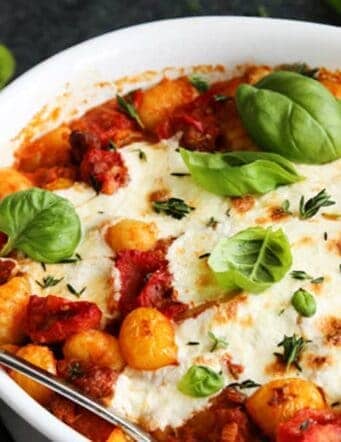 A white bowl of gnocchi with tomato sauce, melted cheese and fresh basil leaves