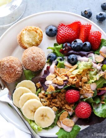 breakfast salad on a white plate topped with granola, served with berries and bananas