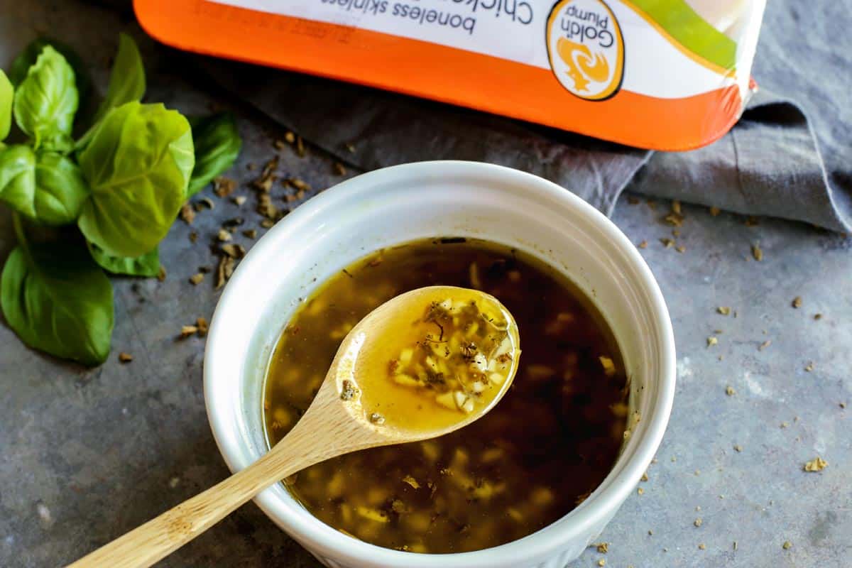 These grilled chicken skewers pair tender marinated strips of grilled chicken with a tangy green curry sauce. The perfect summer dinner! Spoonful of chicken marinade held over bowl