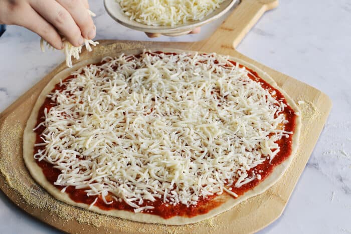 adding shredded mozzarella cheese on top of the pizza sauce