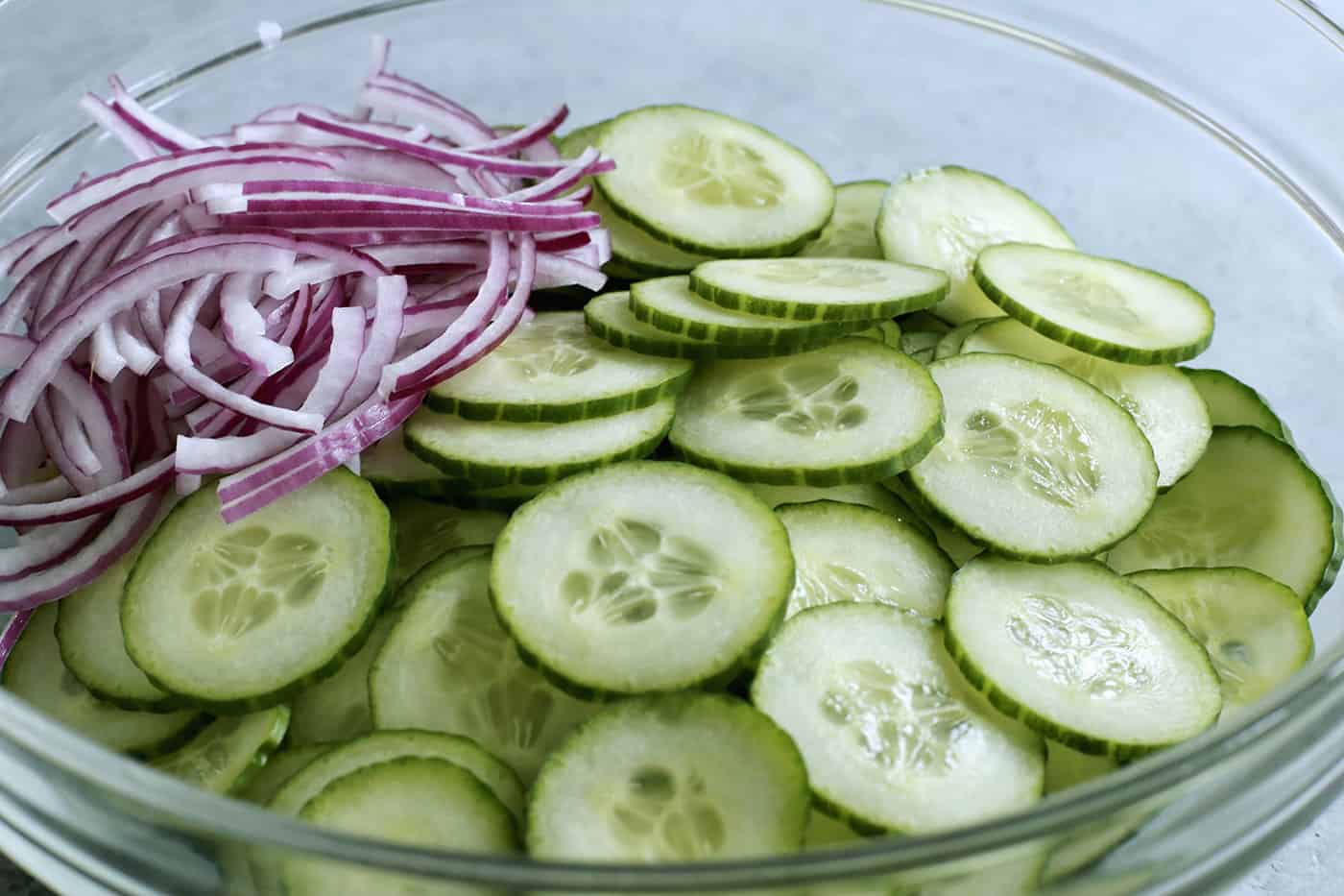 close-up photo of cucumber and red onion slices in a clear bowl