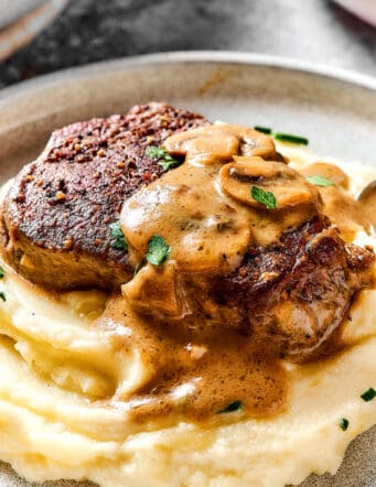 a steak with creamy mushroom sauce over mashed potatoes