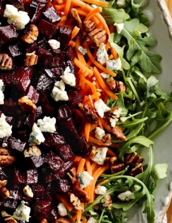 a large platter of salad with arugula, carrots, and roasted beets