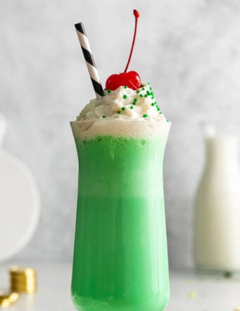 a tall glass with a green mint shake that is topped with whipped cream and a cherry