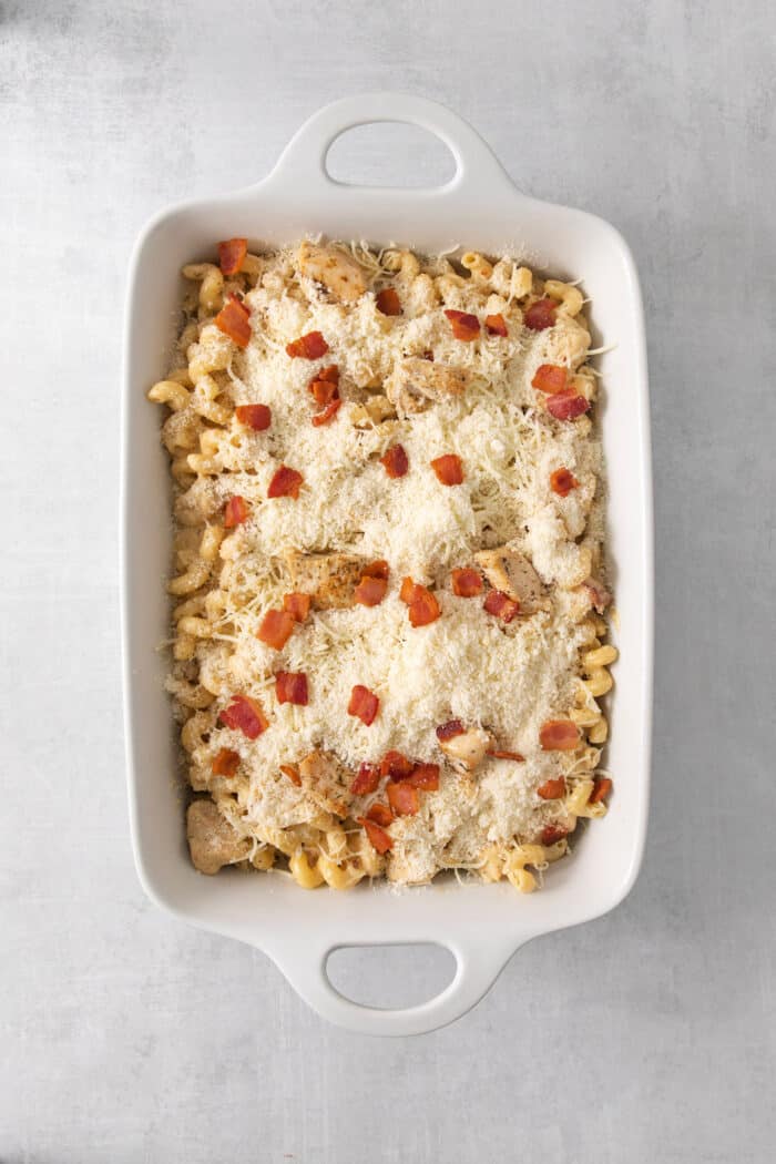 Chicken ranch pasta in a baking dish is covered with cheese and bacone.