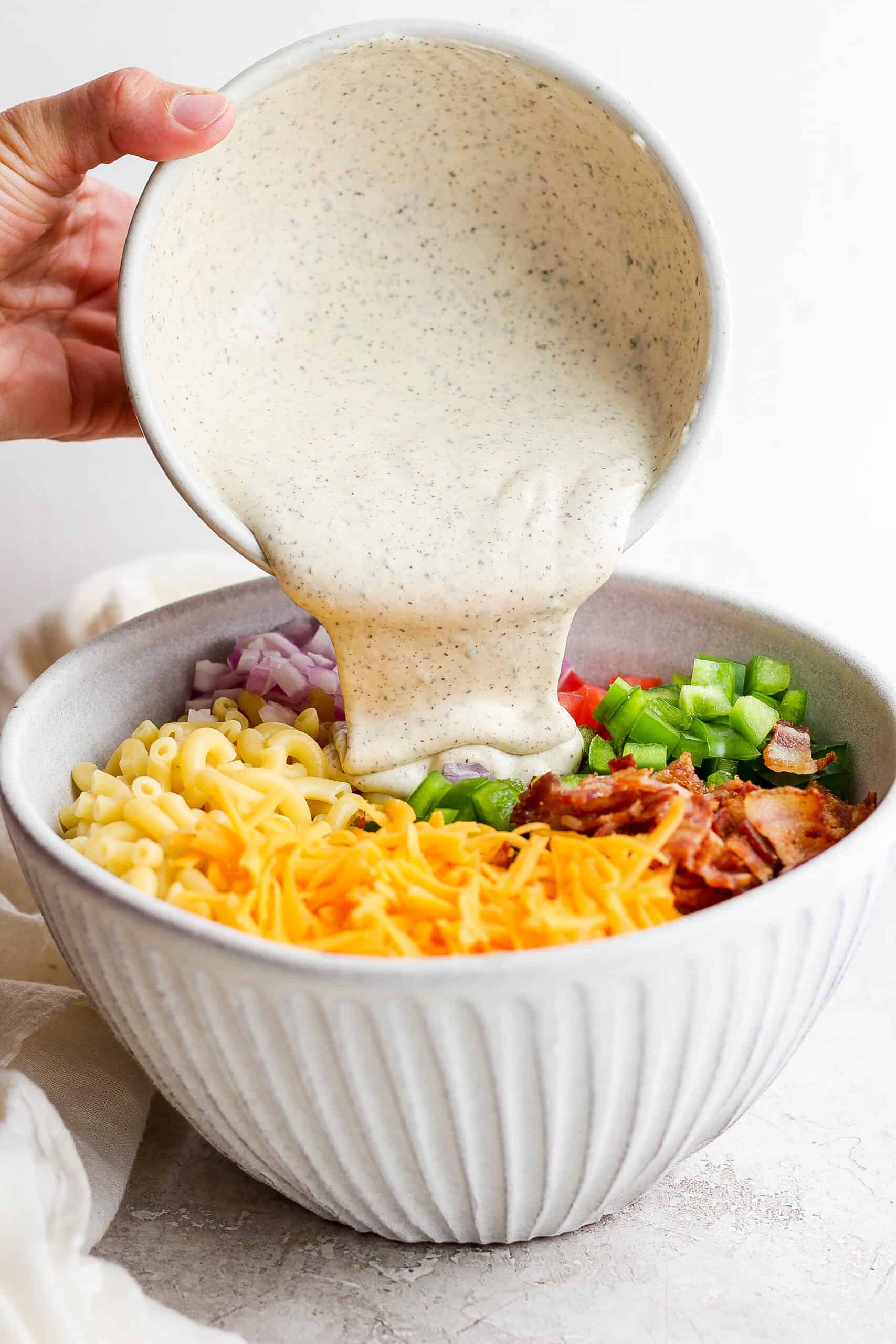 Dressing is poured into a bacon ranch pasta salad.