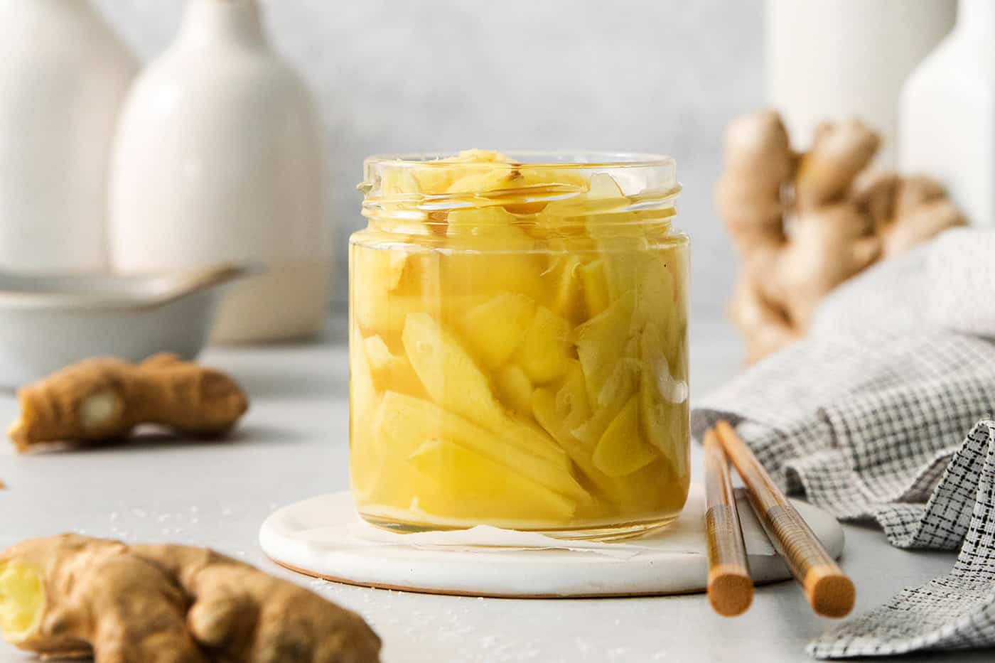 A jar of pickled ginger with ginger in the background.