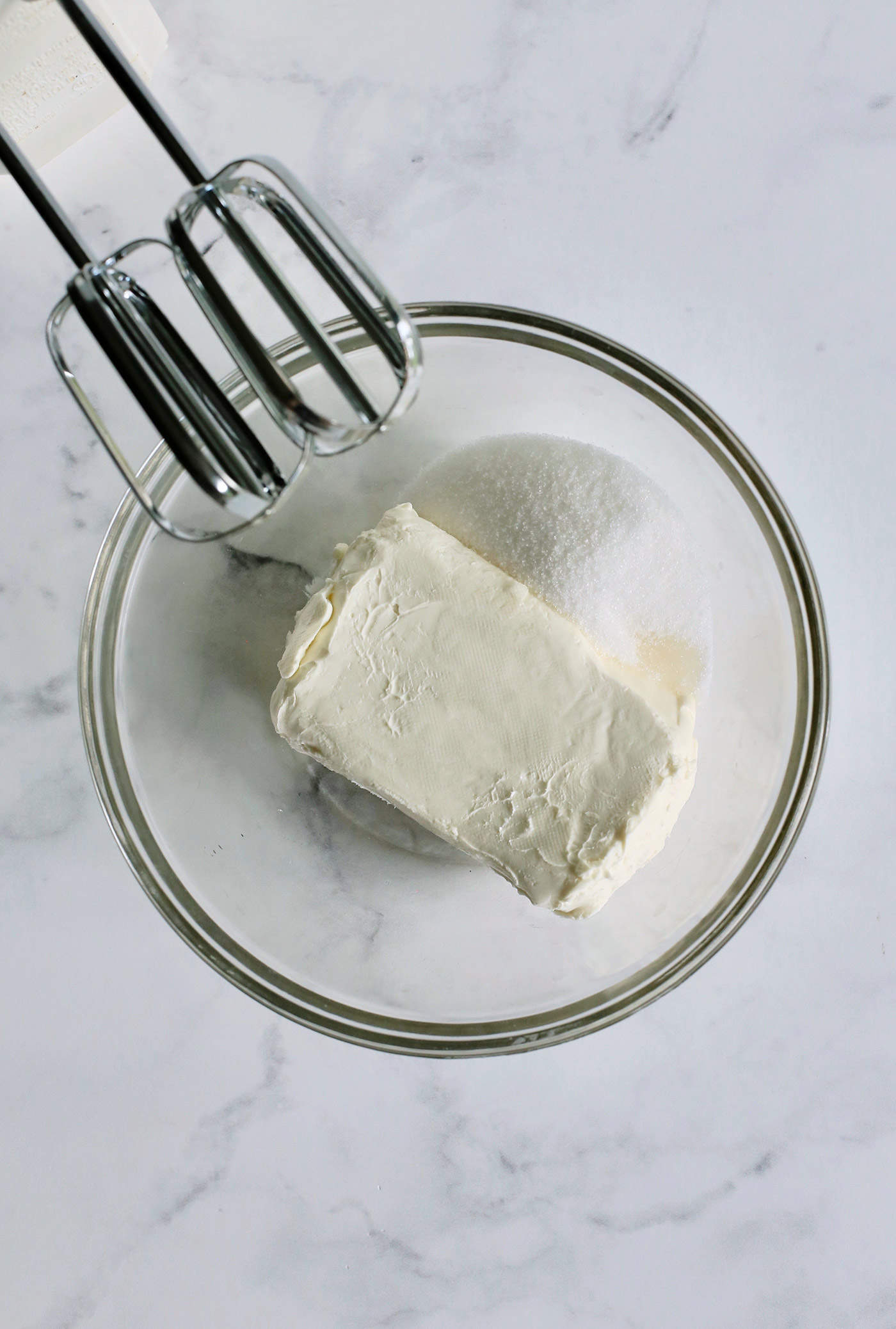 a mixer, plus a clear bowl with sugar, vanilla, and a block of cream cheese