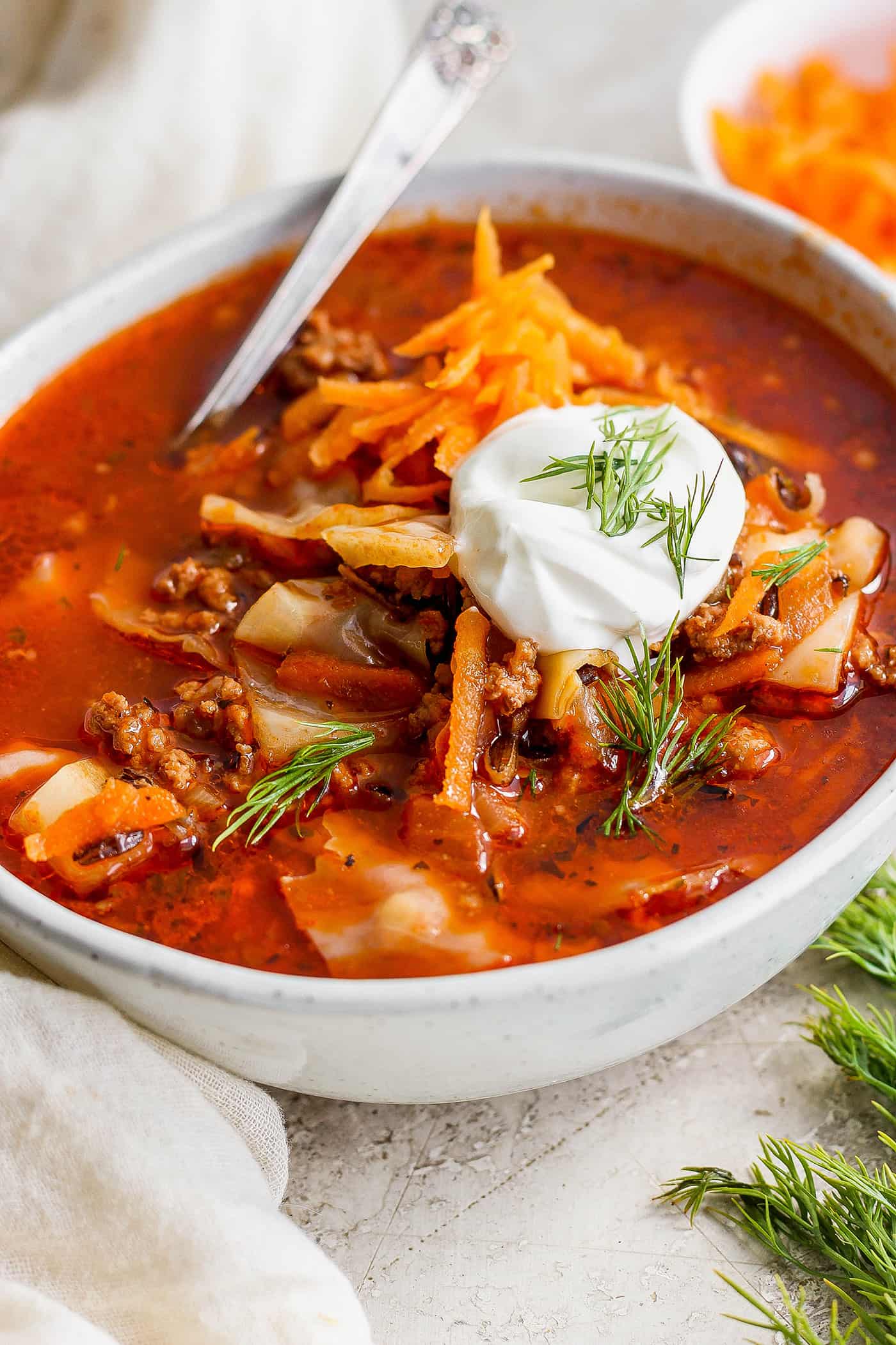 A bowl of unstuffed cabbage roll soup topped with carrot garnish and sour cream.
