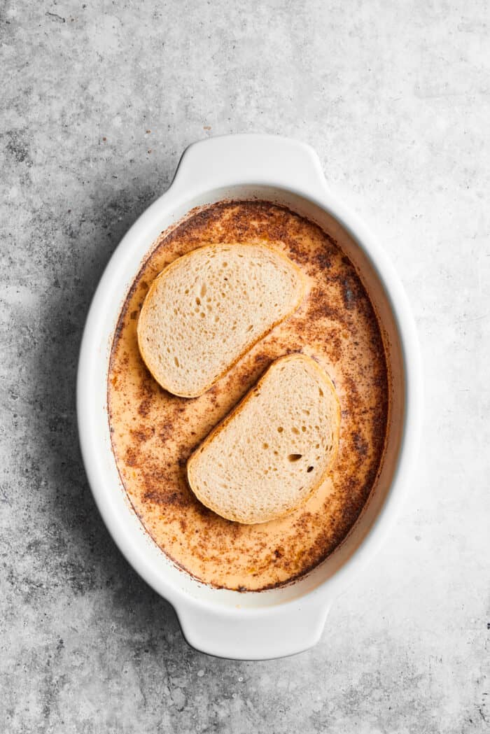 Two slices of bread are dipped in French toast batter in an oval baking dish.