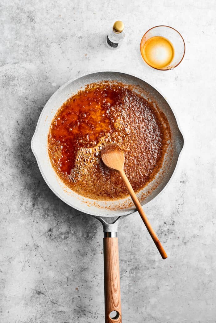 Ground spices are stirred into a skillet of melted butter with a wooded spoon.