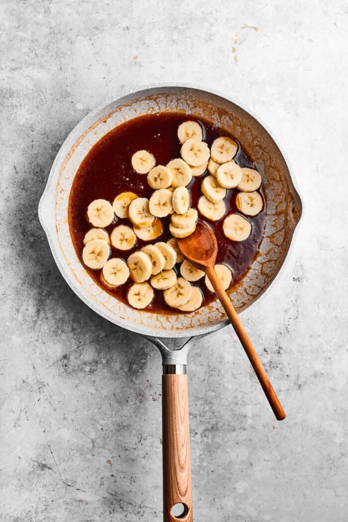 Banana slices cook in a mix of melted butter, maple syrup, rum, and spices in a skillet.