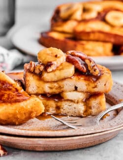 A plate of bananas foster French toast that has been cut into, with more French toast in the background.