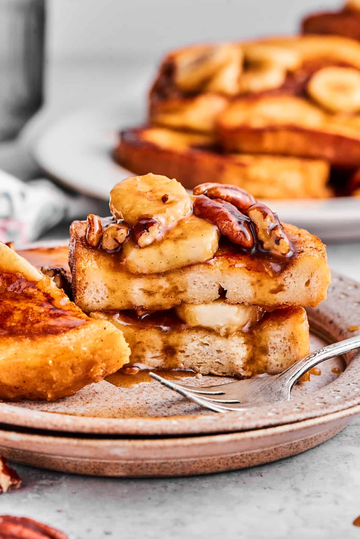 A plate of bananas foster French toast that has been cut into, with more French toast in the background.
