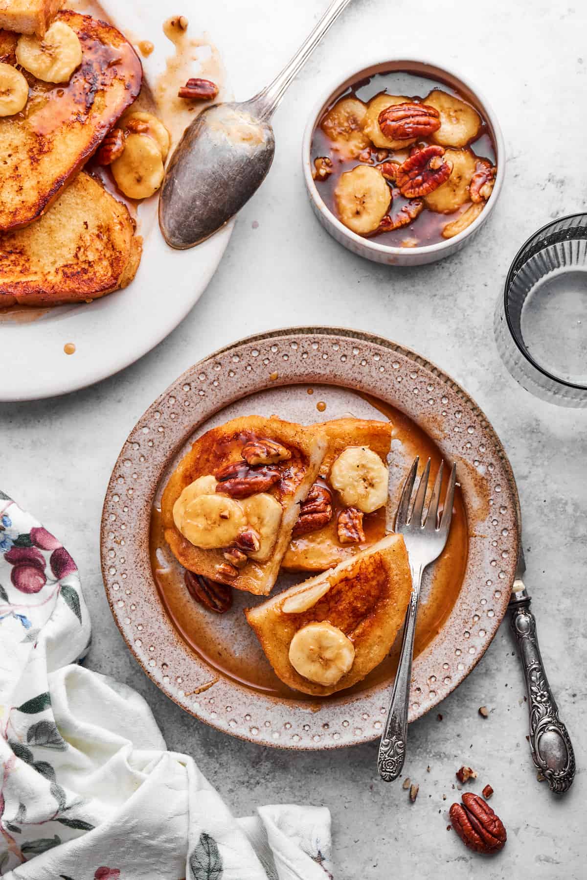 A plate of bananas foster French toast with a fork and a small bowl of bananas in sauce nearby, with more french toast to the left.