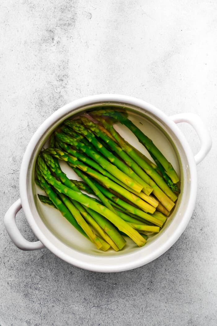 Asparagus spears blanch in a white pot.