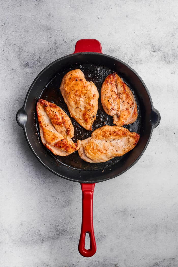 Four pieces of chicken breast brown in a skillet.