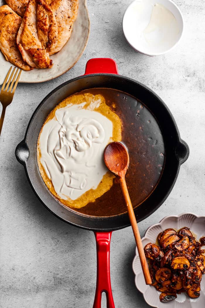A wooden spoon stirs cream into a skillet to make sauce for chicken madeira.
