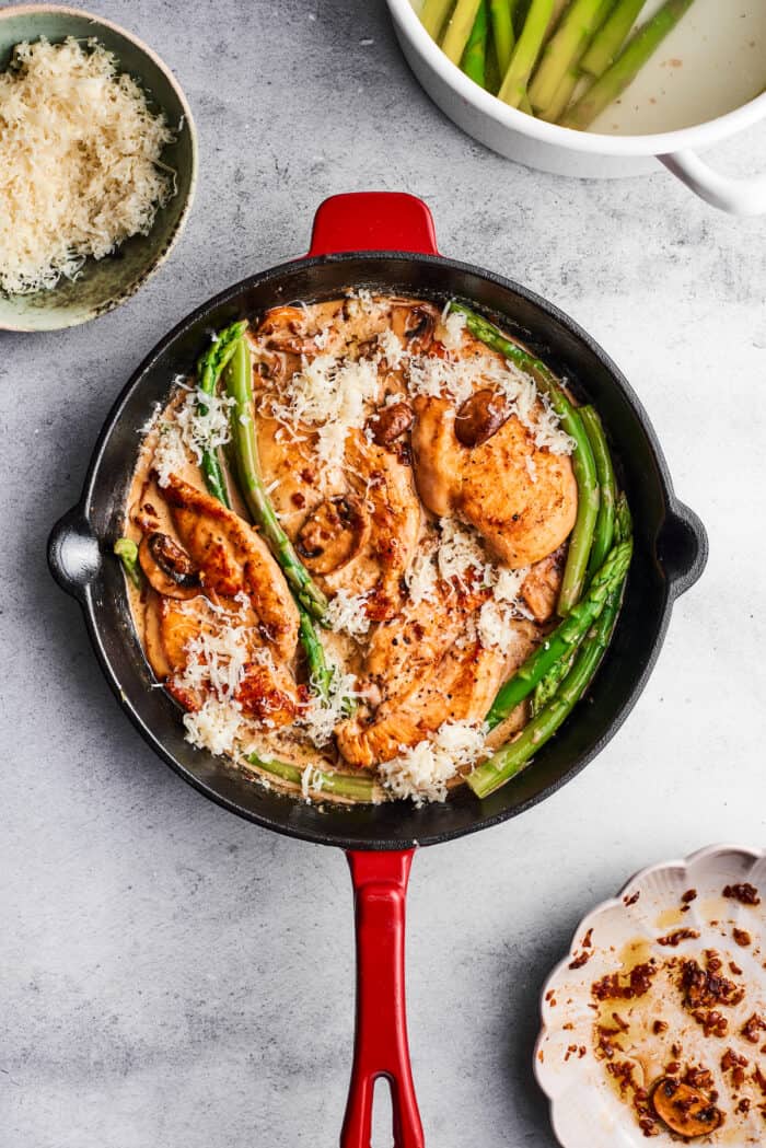 A skillet full of chicken madeira shows asparagus, chicken breast, mushrooms, and cream sauce.