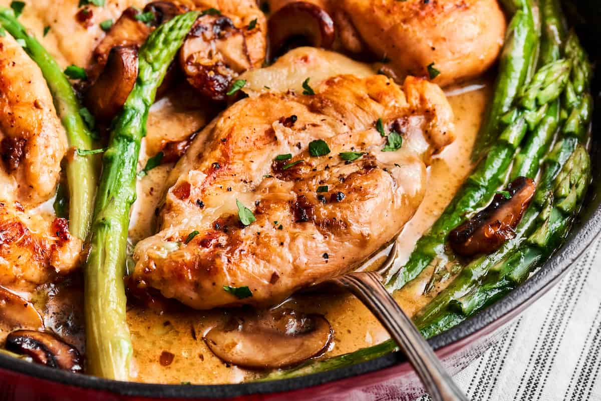 A serving utensil lifts out a piece of chicken from a creamy pan of chicken madeira.