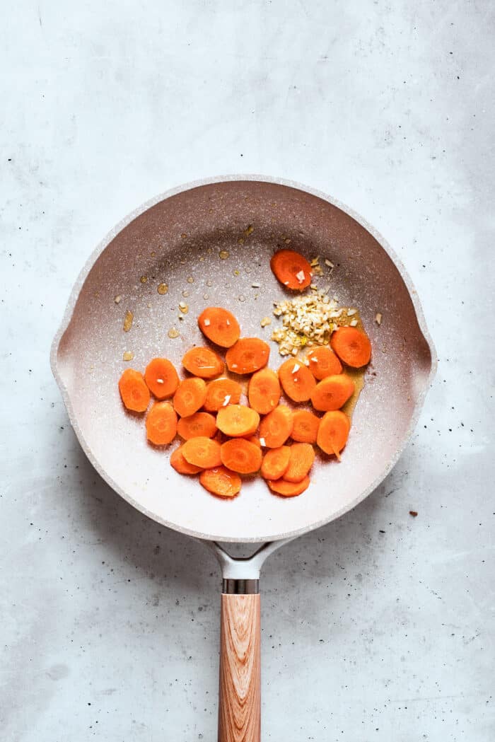 Carrot coins and grated ginger cook in a frying pan.