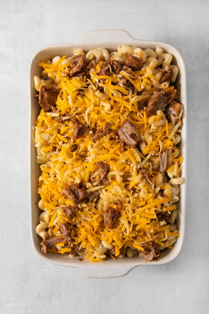 A cheese-topped casserole dish of pulled pork mac and cheese before going in the oven.