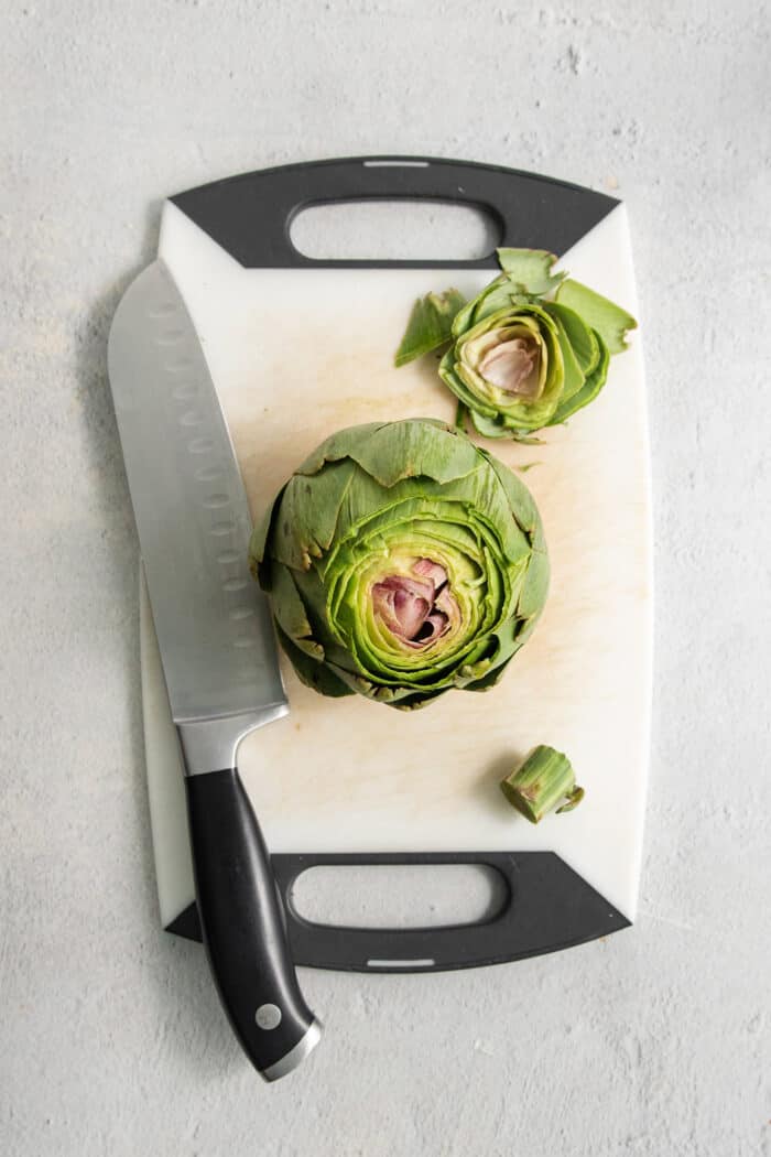 The top and stem are trimmed off of an artichoke.