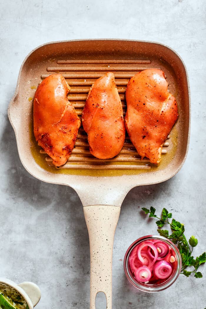 Three chicken breasts cook on a grill pan.