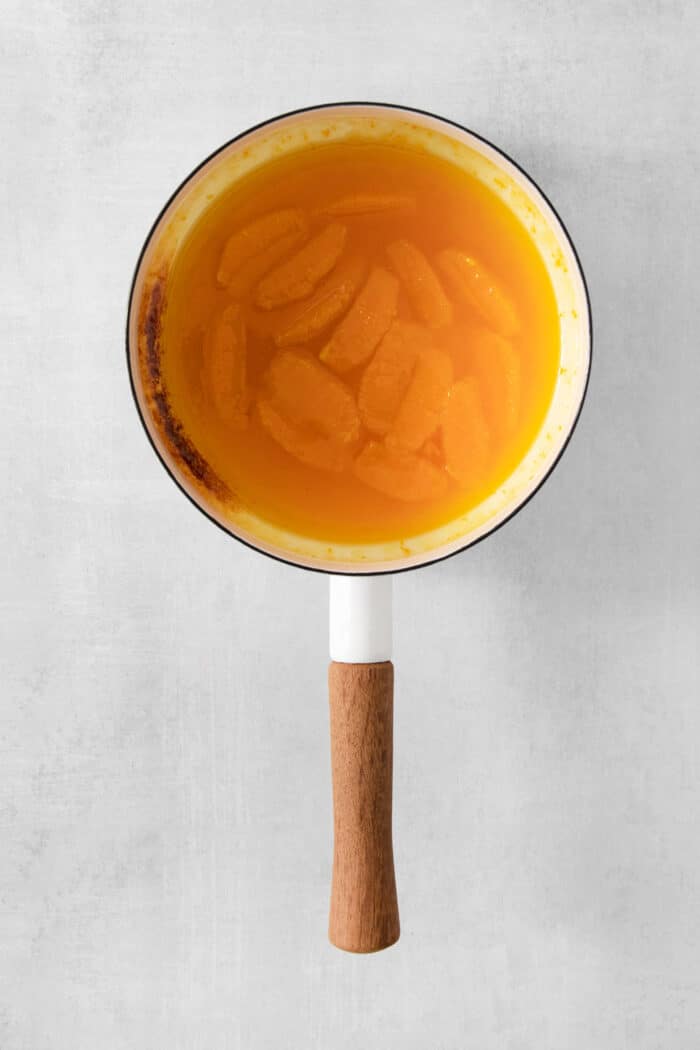Orange segments are added to the pot of orange sauce.