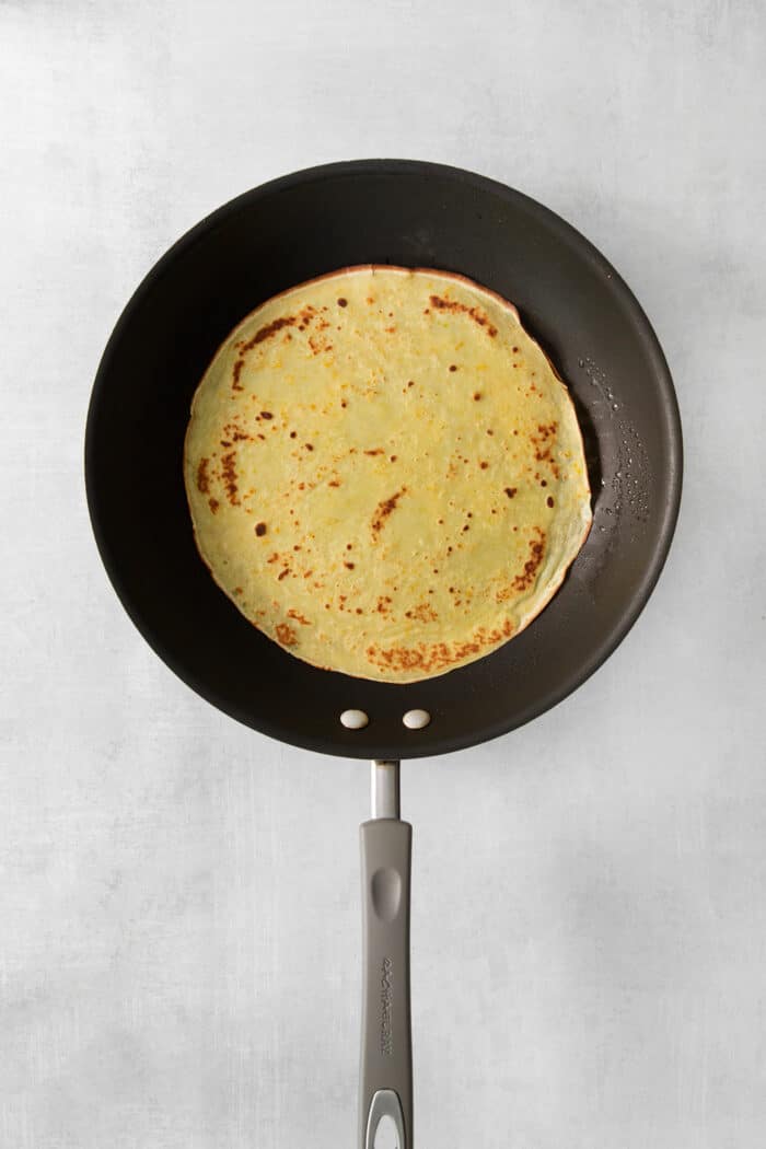 A crepe cooks in a pan.