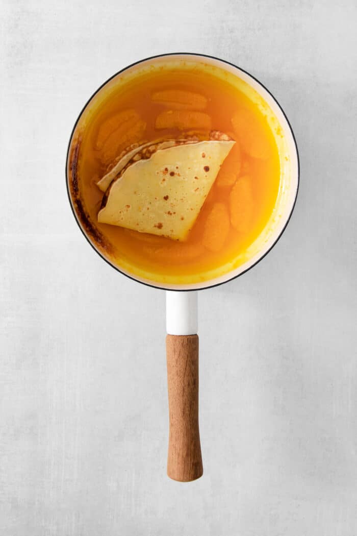 A crepe is added to a pot of orange sauce.