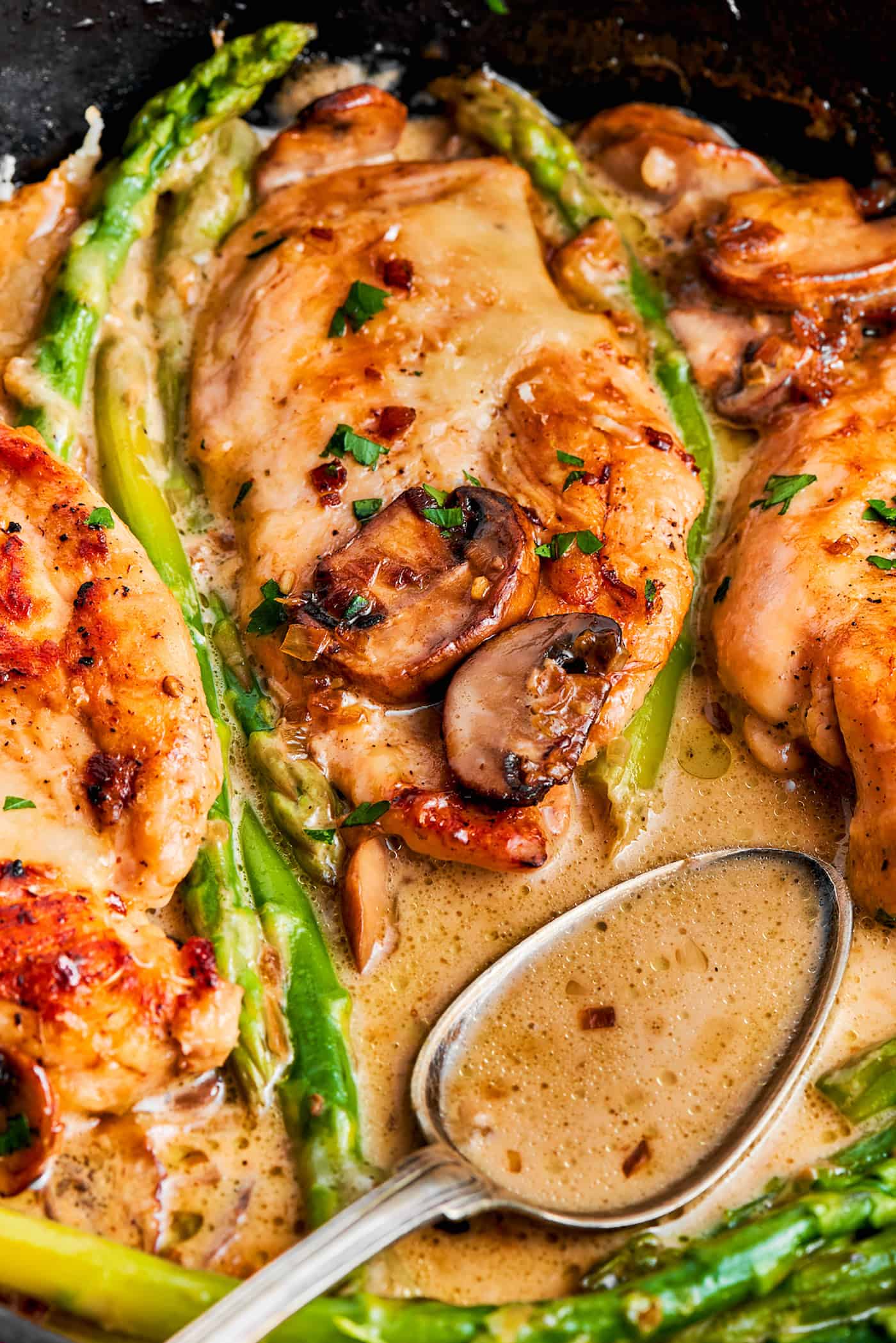 chicken breasts and asparagus in a skillet, with a spoon full of Madeira sauce