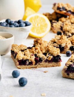 Blueberry crumble bars surrounded by fresh lemons and bowls of blueberries.