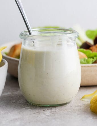 a small jar of Caesar dressing and a salad behind it