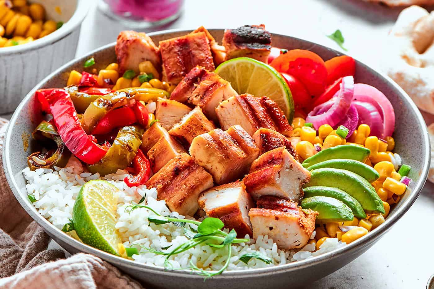 up-close photo of a fajita bowl with rice, chicken, corn salsa, pickled red onions, peppers, and avocado