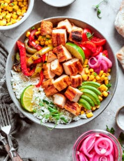 a chicken fajita bowl with rice, corn salsa, pickled red onions, peppers, and avocado