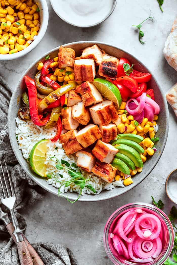 a chicken fajita bowl with rice, corn salsa, pickled red onions, peppers, and avocado