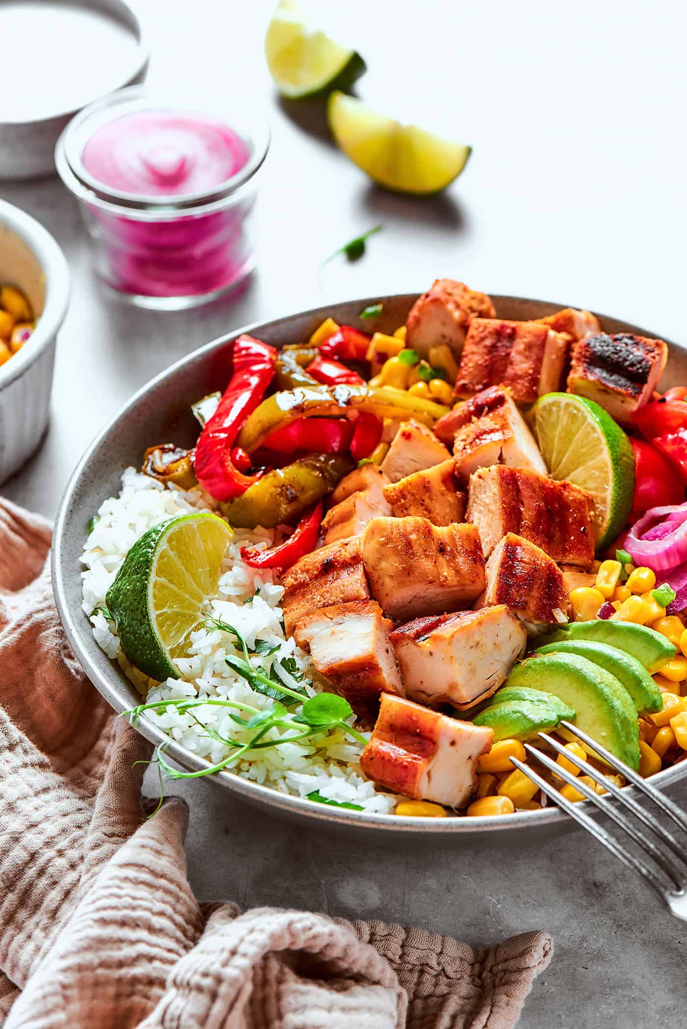 a fajita bowl with rice, chicken, corn salsa, pickled red onions, peppers, and avocado