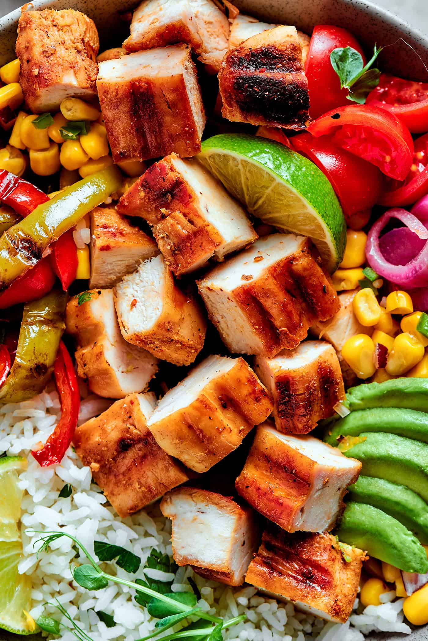 overhead photo of a fajita bowl with rice, chicken, corn salsa, pickled red onions, peppers, and avocado