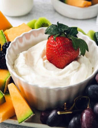 A strawberry is dipped into a bowl of fruit dip.