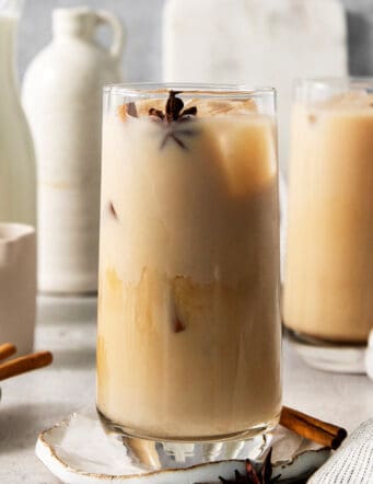 A tall glass of iced chai latte with another in the background.