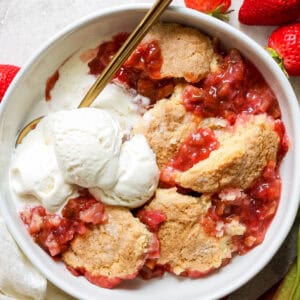 a bowl of rhubarb and strawberry cobbler with scoops of vanilla ice cream