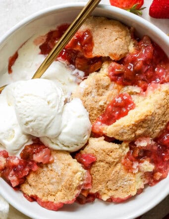 a bowl of rhubarb and strawberry cobbler with scoops of vanilla ice cream