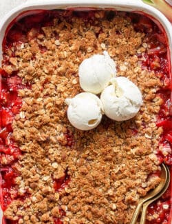 strawberry rhubarb crisp in a white rectangular baking dish, with scoops of ice cream on top